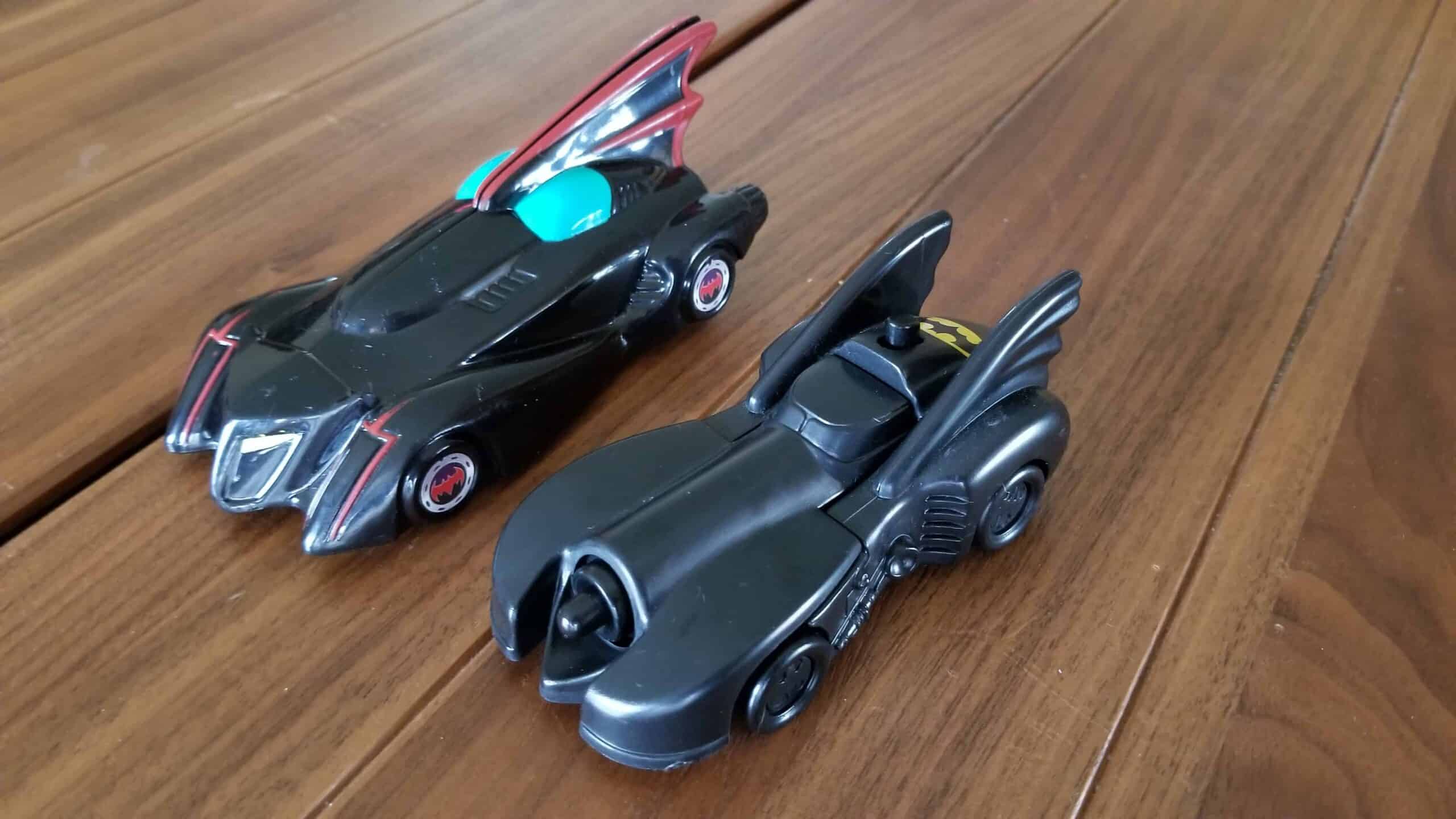 Two different Batman Batmobile toys on a wooden table